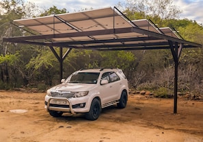 Ein weißer SUV steht unter einer solarbetriebenen Markise in einer natürlichen Umgebung.