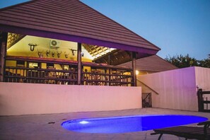 Un área de piscina con una zona de estar cubierta y un edificio con un diseño de techo característico.