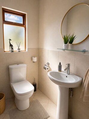 Un baño con inodoro, lavamanos, ventana y espejo.