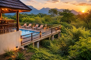A poolside area with lounge chairs, a wooden deck, and a view of mountains.