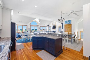 A spacious kitchen with a large island, wooden flooring, and a view of the sea through the windows. - Whit's End: Oceanfront, Private Pool, Elevator, Hot Tub, Theater and Game Room (Nags Head)