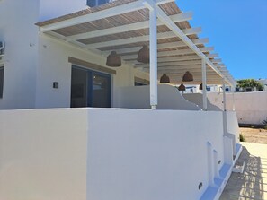 A modern building with a white exterior, a covered outdoor area with hanging baskets, and a door leading to the interior. - ALINTHEA 3, Alinda, Leros (Leros)