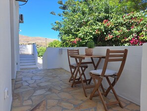Eine Terrasse mit Steinboden, Holzstühlen, einem Tisch und einem Blumentopf.