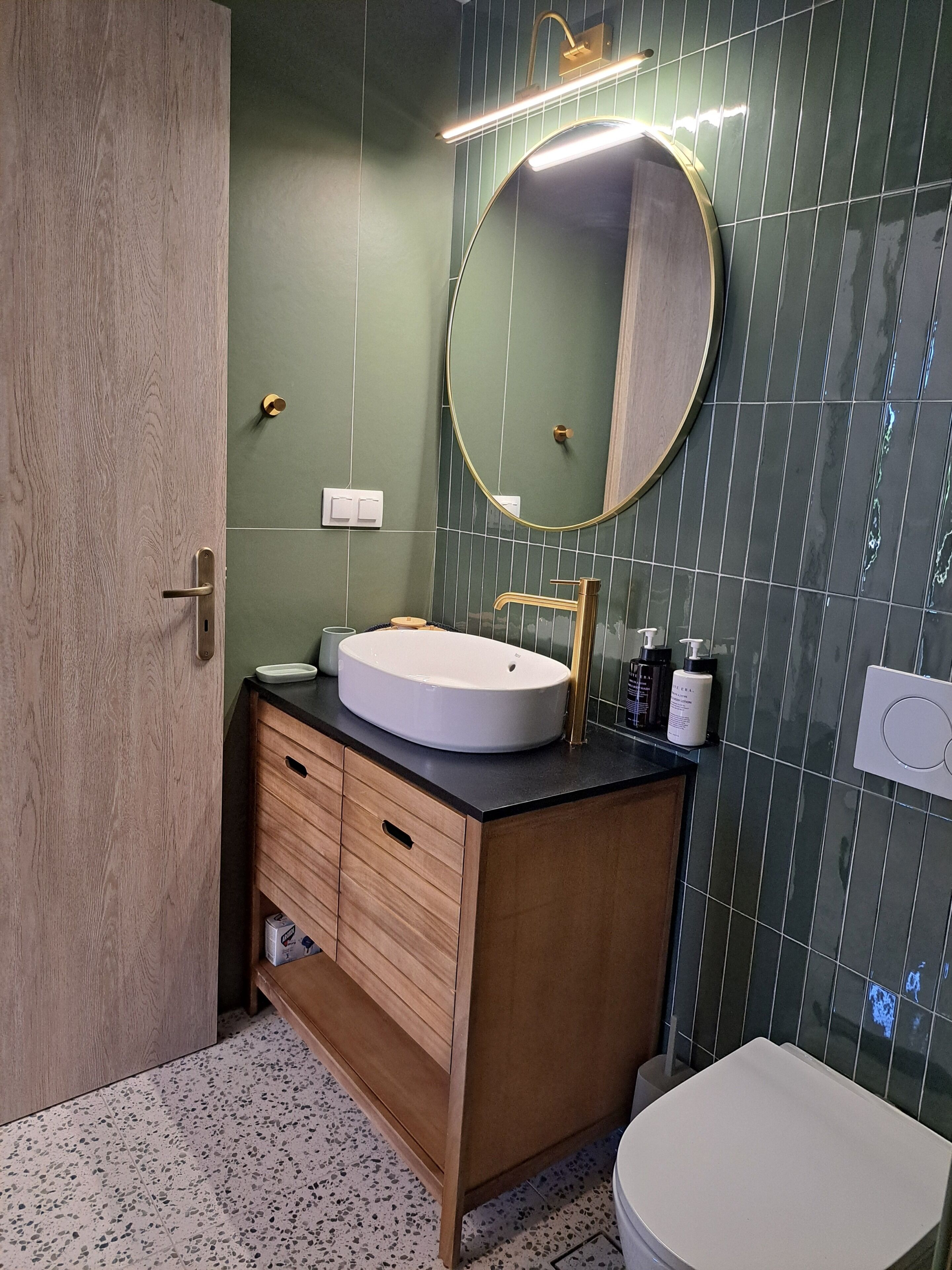Ein Badezimmer mit einem Holzbadezimmer-Möbel, einem runden Spiegel, einem weißen Waschbecken und einer Toilette.