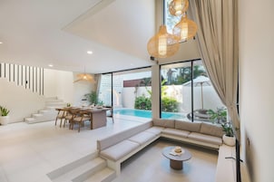 A modern interior with a dining area, a sofa, a pool, and a staircase.