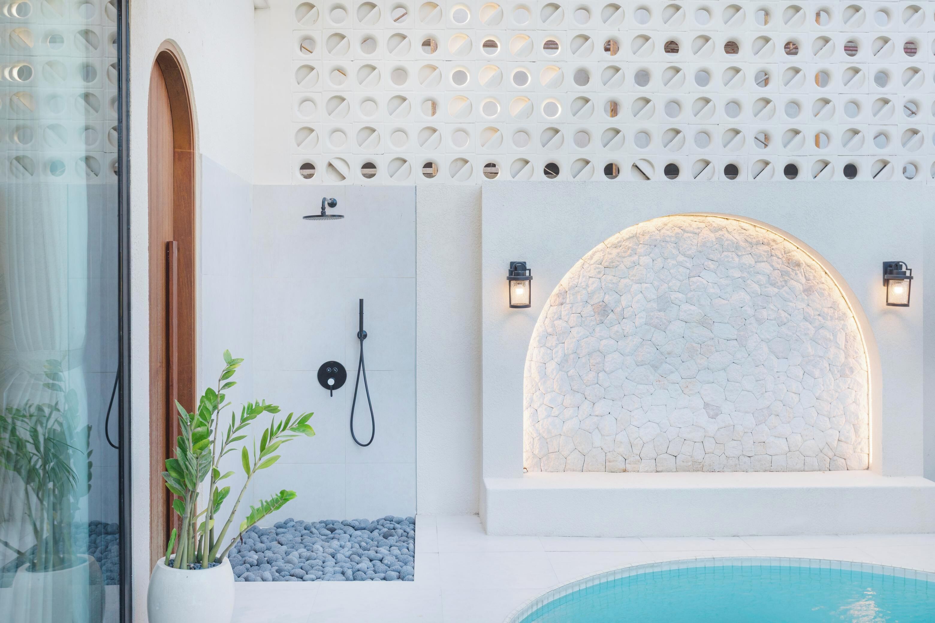 Un baño moderno con cabina de ducha de vidrio, un lavamanos blanco y una pared de piedra con fuente integrada.