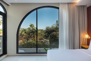 A bedroom with a large window, a bed, a nightstand, and a lamp.