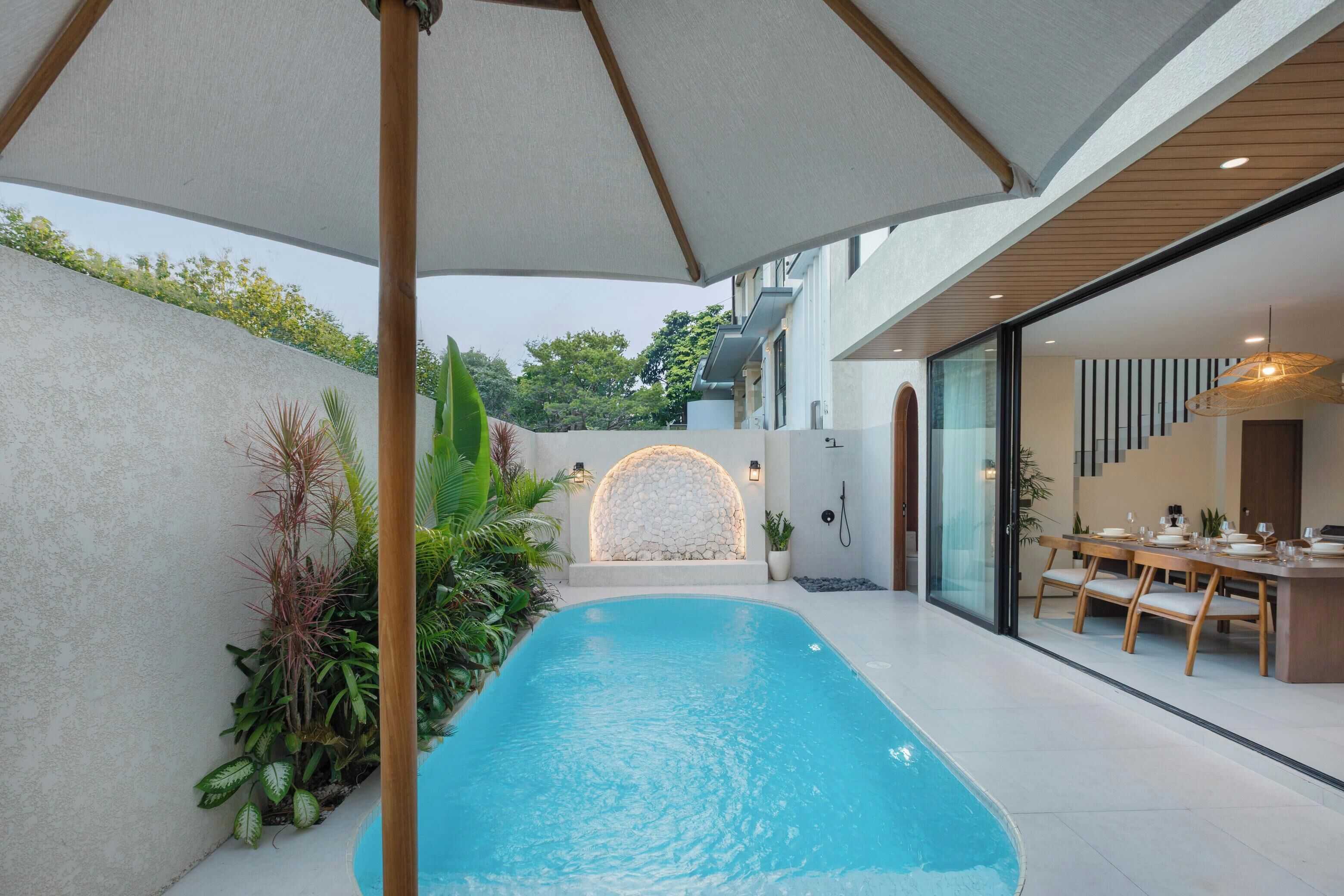 A modern indoor pool area with a clear view of the pool, surrounded by plants and a stone wall.