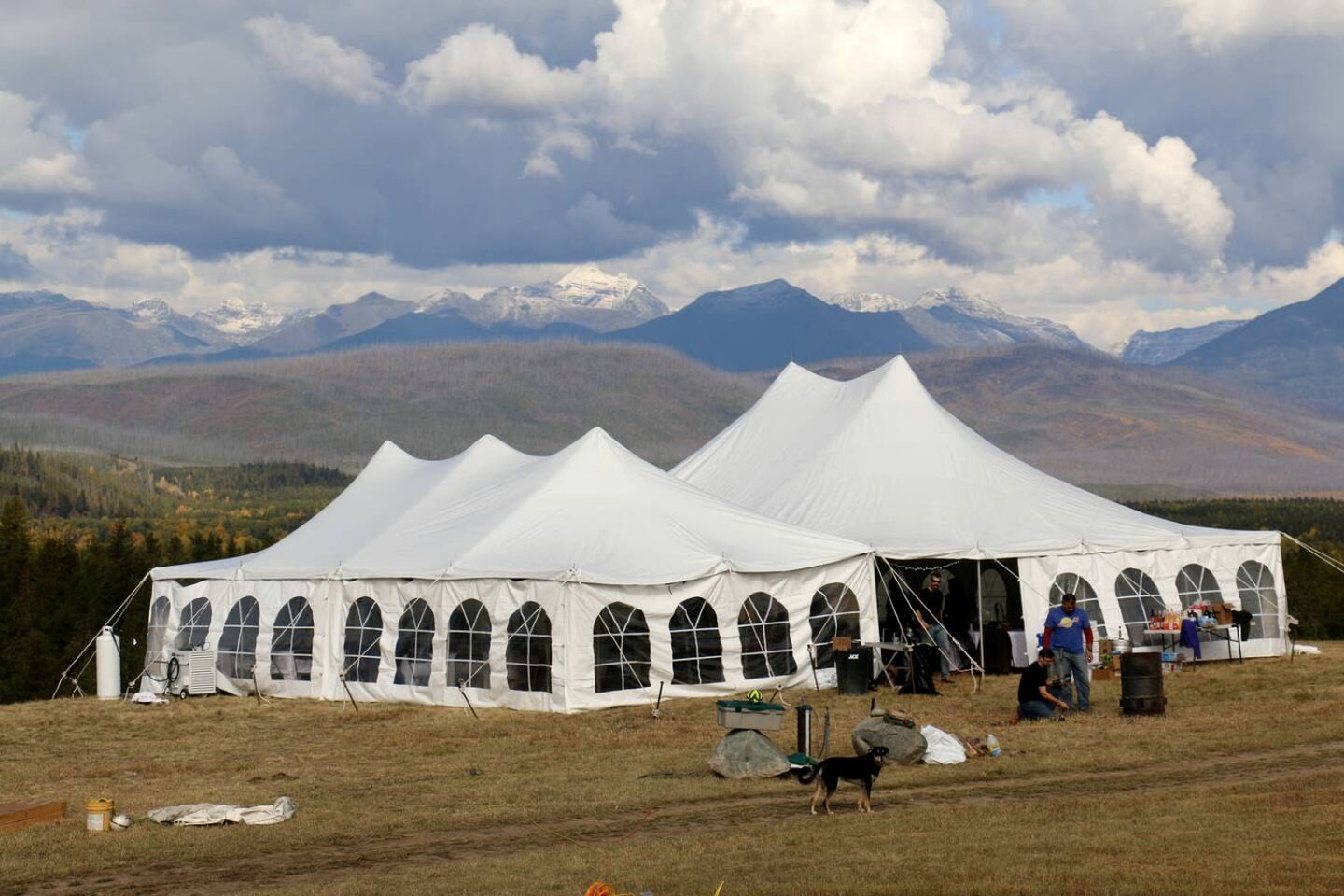 A large white tent with arched windows, set in a grassy field with mountains in the background.