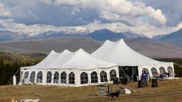 A large white tent with arched windows, set in a grassy field with mountains in the background.