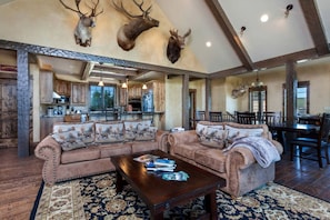 A spacious living room with a large sectional sofa, a coffee table, and a dining area with wooden chairs.