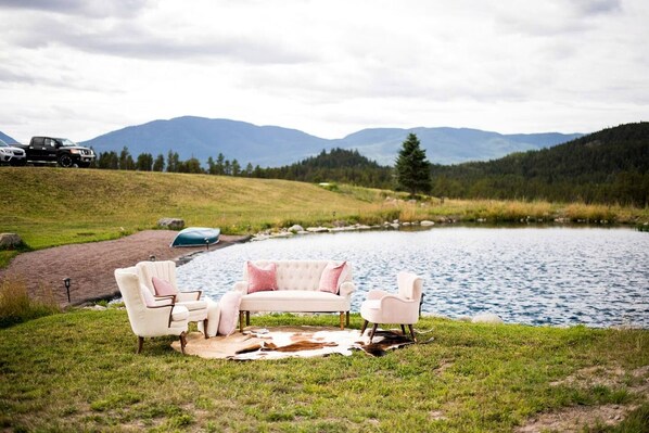 A lakeside setting with a white couch and chairs, a blanket, and a canoe.