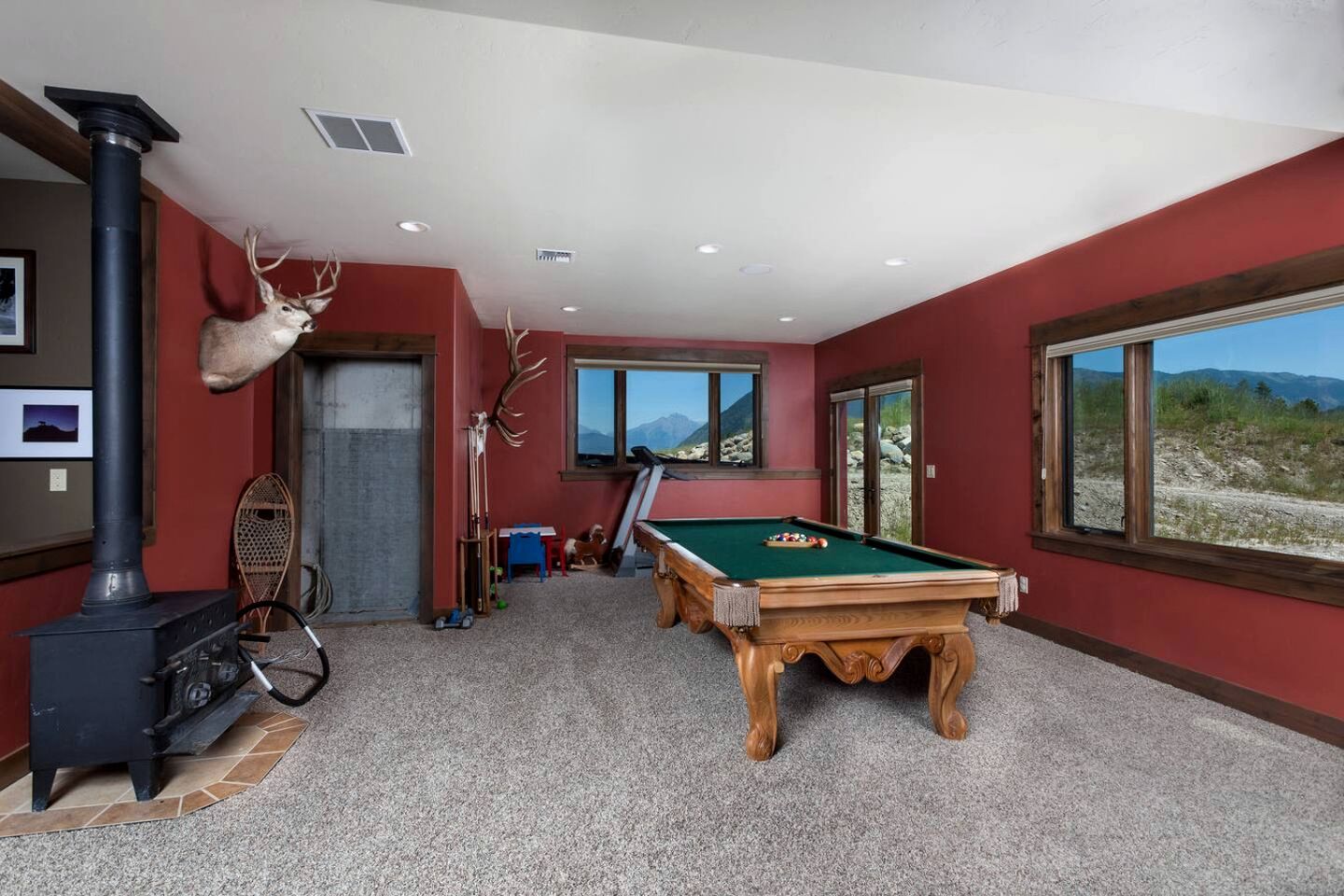 Ein Zimmer mit Pooltisch, Kamin und großen Fenstern mit Blick auf die Berge.