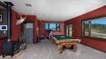 Ein Zimmer mit Pooltisch, Kamin und großen Fenstern mit Blick auf die Berge.