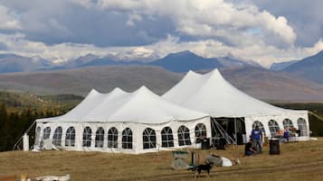 Une grande tente blanche aux fenêtres en arc de cercle, installée dans un champ verdoyant avec des montagnes en arrière-plan.