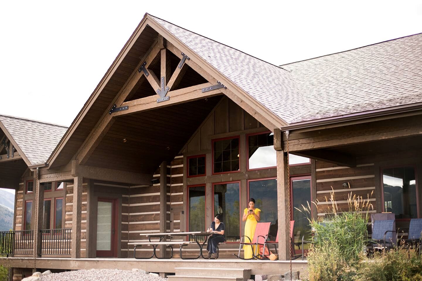 A wooden lodge with a covered porch, large windows, and a picnic table.