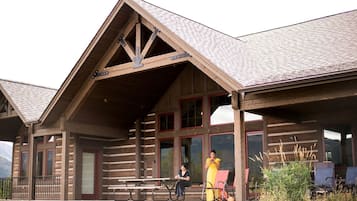 A wooden lodge with a covered porch, large windows, and a picnic table.
