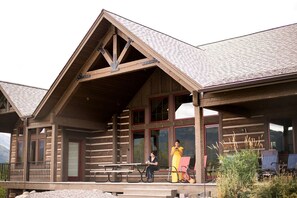 A wooden lodge with a covered porch, large windows, and a picnic table.