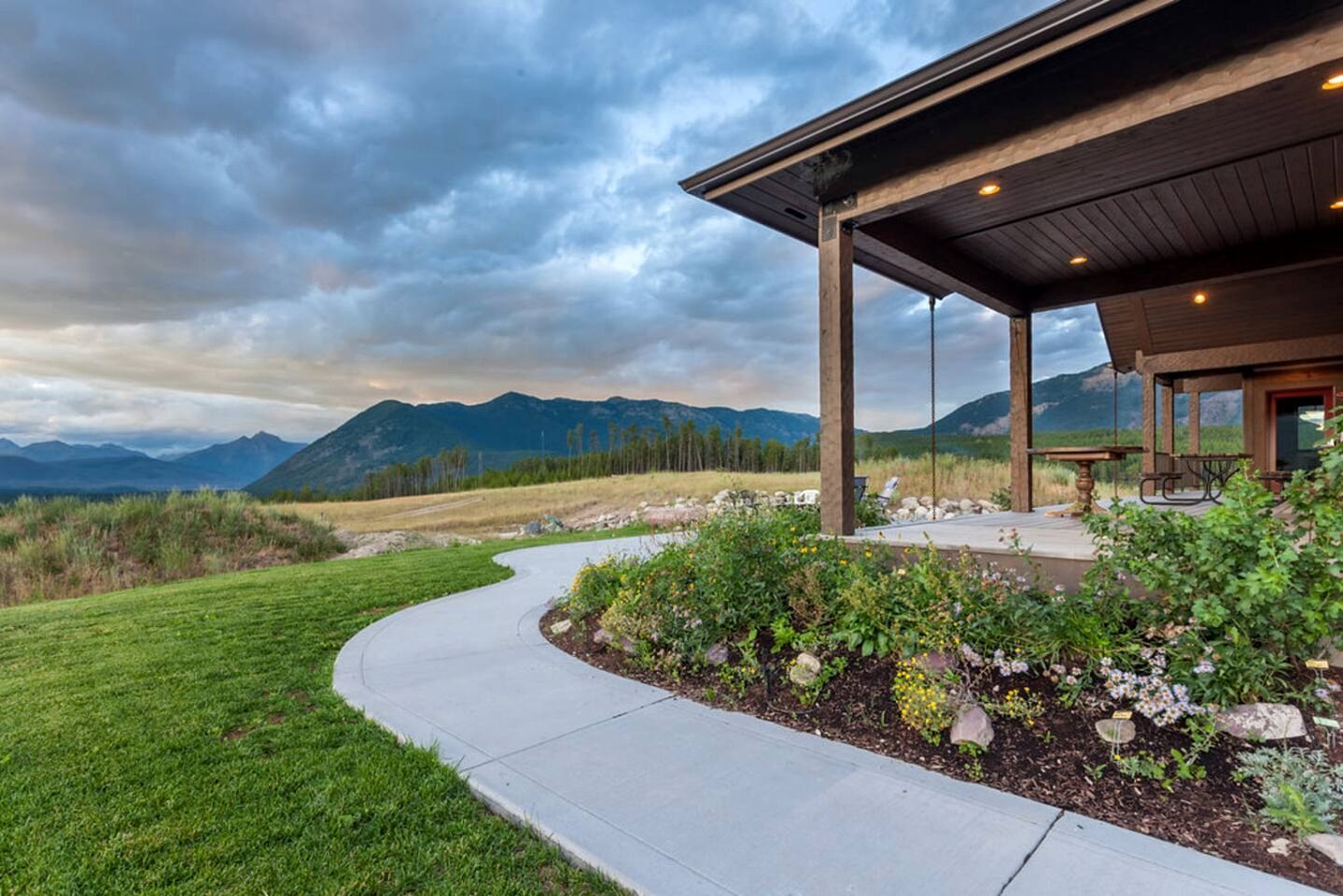 A building with a covered patio, a curved pathway, and a mountainous backdrop.