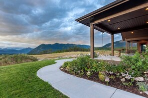 A building with a covered patio, a curved pathway, and a mountainous backdrop.