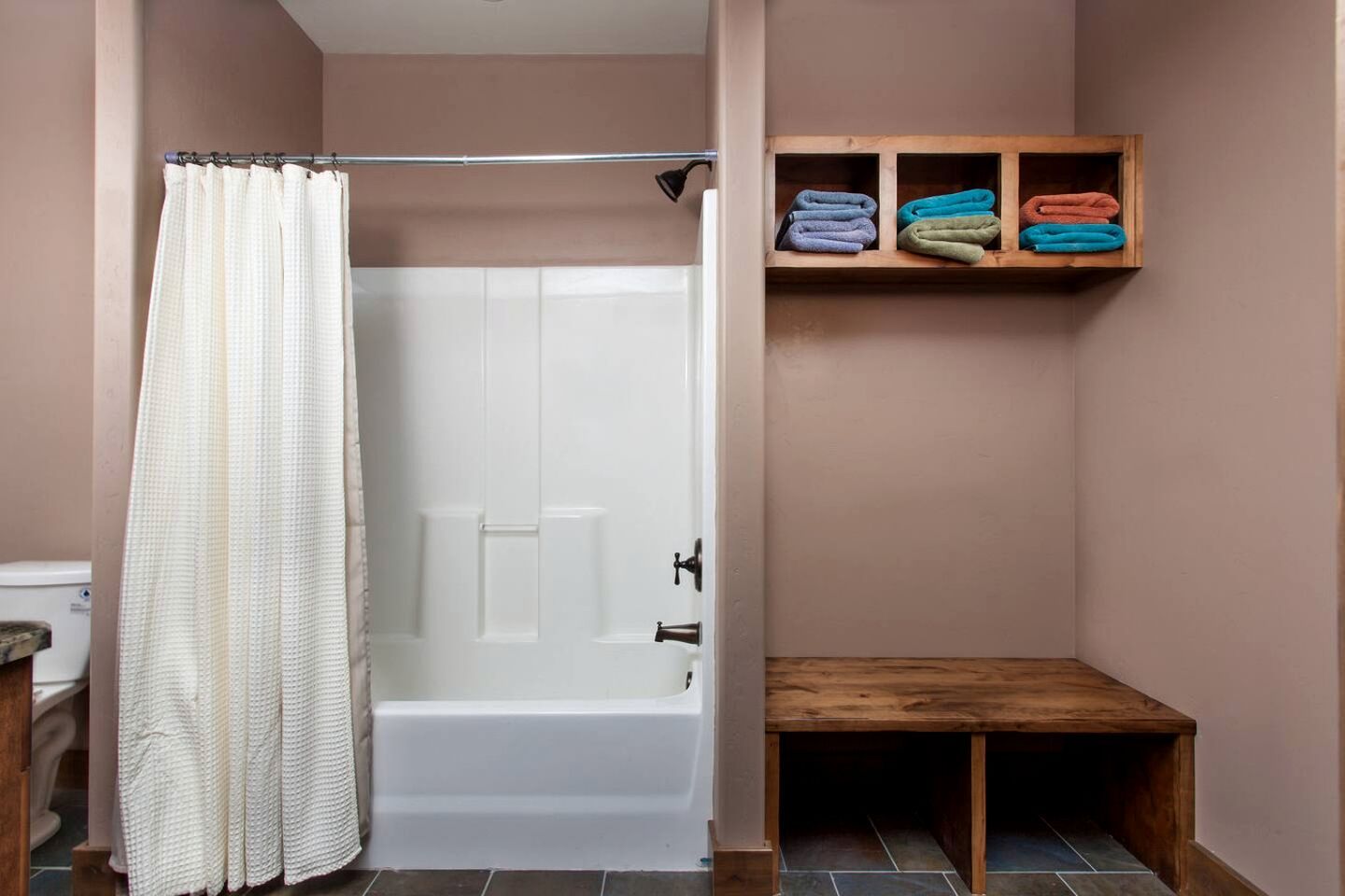 A bathroom with a shower curtain, a bathtub, and a shelf with folded towels.