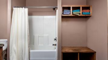 A bathroom with a shower curtain, a bathtub, and a shelf with folded towels.