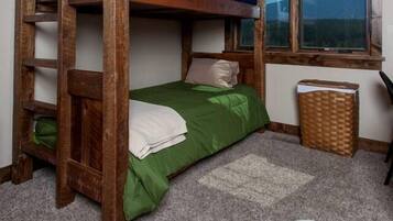 A bunk bed room with a window, a desk, and a trash bin.