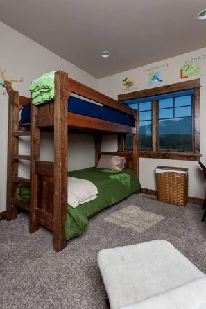 A bunk bed room with a window, a desk, and a trash bin.