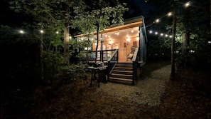 Eine kleine Holzhütte mit einer Treppe, die zu einer Terrasse führt, umgeben von Bäumen und Lichterketten.