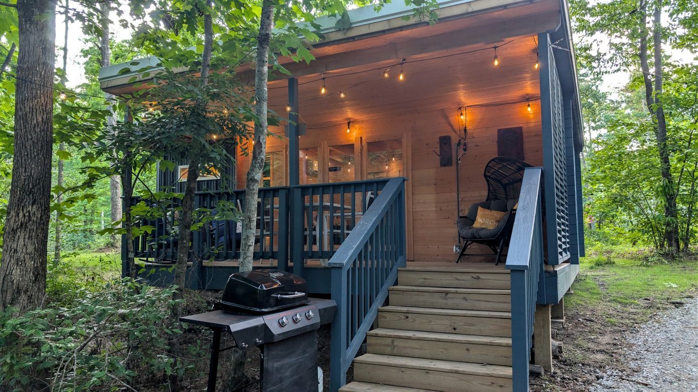 A wooden deck with a grill, a chair, and a staircase leading to an upper level.