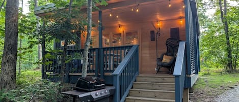 A wooden deck with a grill, a chair, and a staircase leading to an upper level.