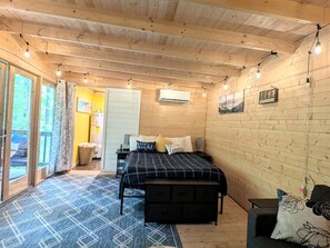 Ett rum med träpanel på väggarna, en säng, en bänk, ett litet bord och en skjutdörr i glas som leder ut.