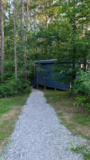 Ein Kiesweg führt zu einer blauen Struktur, umgeben von Bäumen.