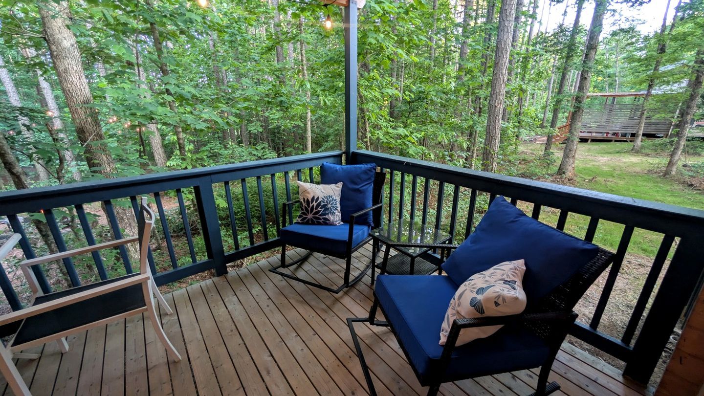 A wooden deck with two blue cushioned chairs and a bench, surrounded by a black railing.