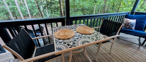 A wooden deck with a table and chairs, a bench, and a view of a forest.