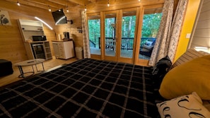 Een houten slaapkamer met een bed, een klein bureau, een televisie en een balkon met uitzicht op bomen.
