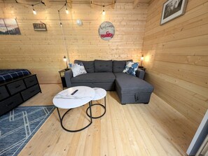 Ett mysigt rum med en grå hörnsoffa, ett litet runt bord och en blå, mönstrad matta.