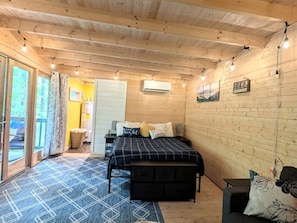 Ein Zimmer mit Holzwänden, einem Bett, einer Bank, einem kleinen Tisch und einer Schiebetür zum Außenbereich.