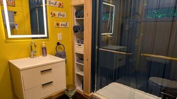 Een badkamer met een gele wand, een witte wastafel, een spiegel, een douchecabine en een toilet.