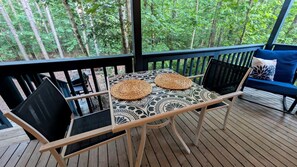 Eine Holzterrasse mit Tisch und Stühlen, einer Bank und Blick auf einen Wald.