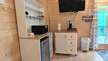 Ein Zimmer mit Holzwänden, einem an der Wand befestigten Fernseher, einem kleinen Schrank, einer Mikrowelle und einem Mülleimer.