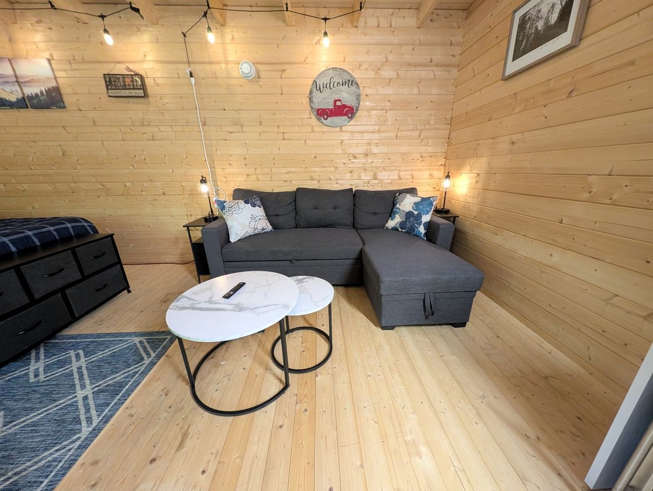 Ein gemütlicher Raum mit einem grauen Ecksofa, einem kleinen runden Tisch und einem blauen Teppich mit Muster.