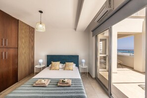 Ein Schlafzimmer mit Bett, Nachttischen, einer Hängeleuchte, Meerblick und einem Balkon.