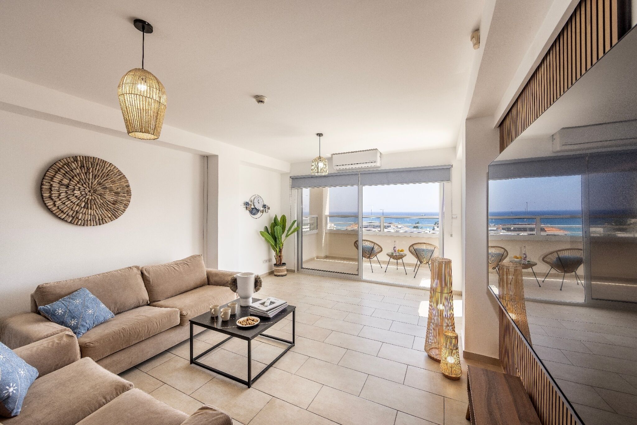 Un salon spacieux, doté d’un canapé, d’une table basse et d’objets décoratifs. Une grande fenêtre offre une vue sur la plage.