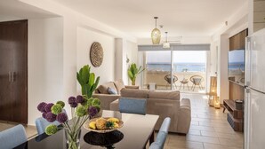 A modern living room with a sofa, dining table, and chairs, a kitchen area, and a balcony with a view of the sea. - 3 Bedroom Penthouse In the Absolute Center Of Protaras (Paralimni)