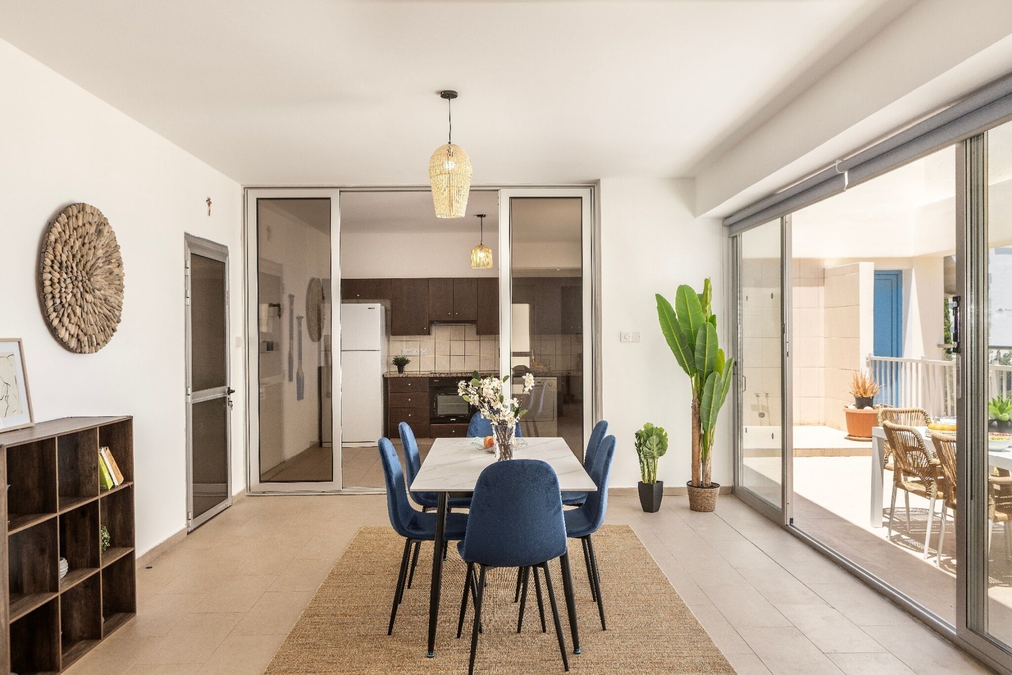 A dining area with a table, chairs, a chandelier, and a view through a glass door to a balcony.