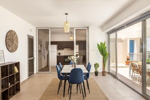 Een eetruimte met een tafel, stoelen, een kroonluchter en een uitzicht door een glazen deur op een balkon.