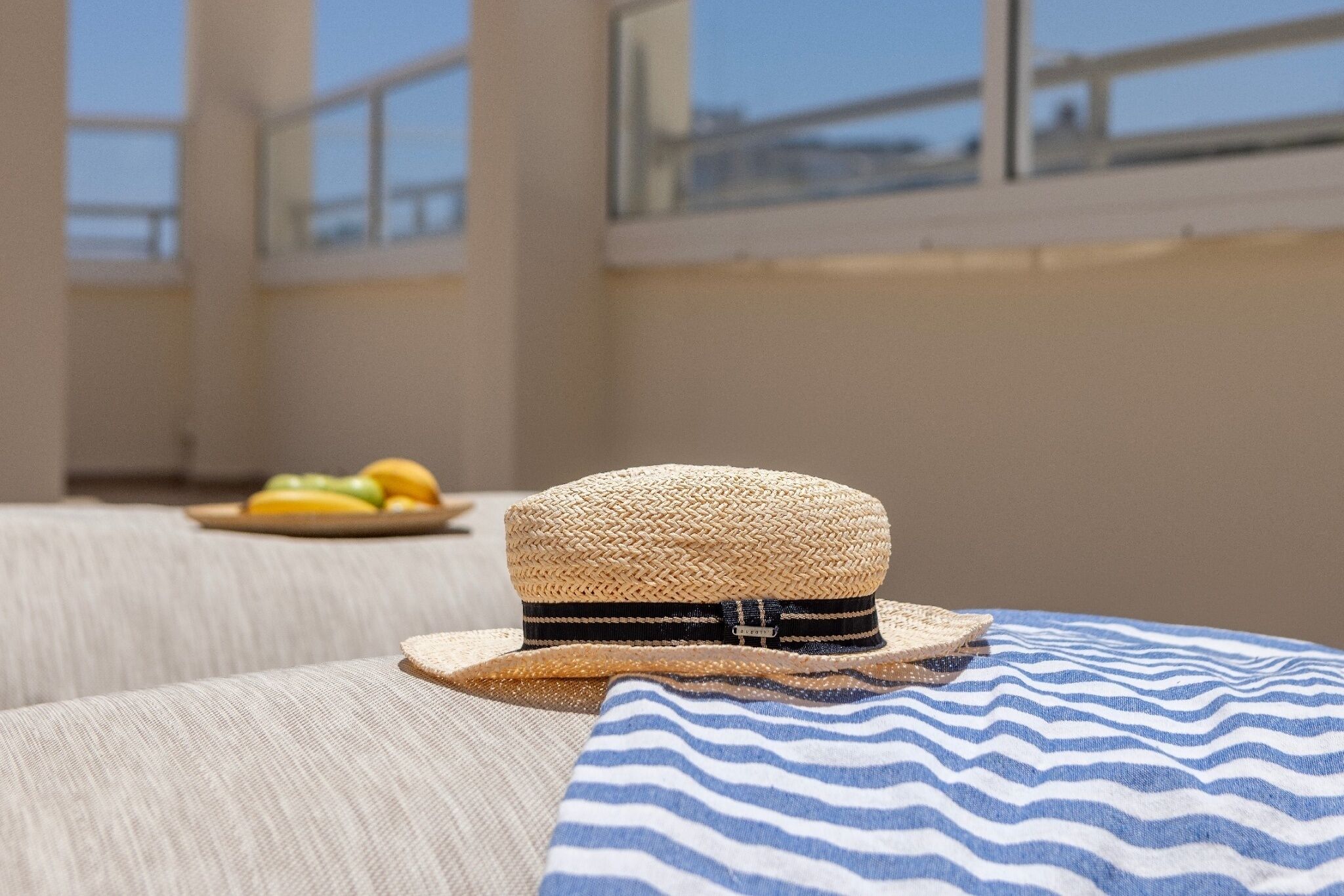A room with a large window, a straw hat on a cushion, and a plate with fruit.