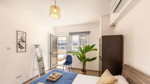 Ein Hotelzimmer mit einem Bett, einer großen Topfpflanze, einem Sessel, einem Spiegel und einer Pendelleuchte.