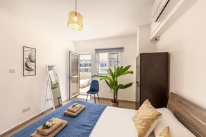 Een hotelkamer met een bed, een grote kamerplant, een stoel, een spiegel en een hanglamp.